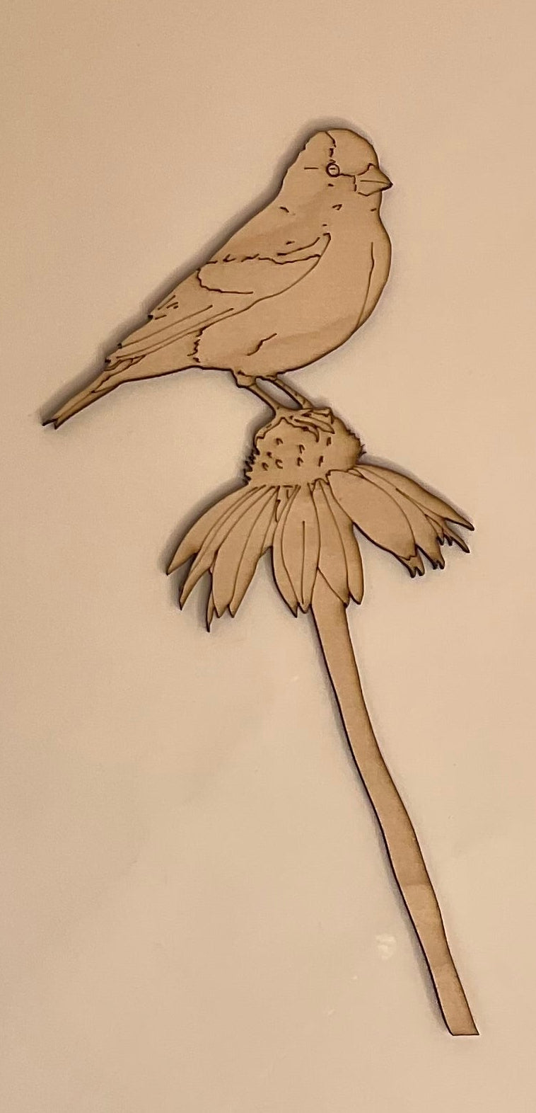 Wooden cutout of a bird on a branch with a flower on a white surface.